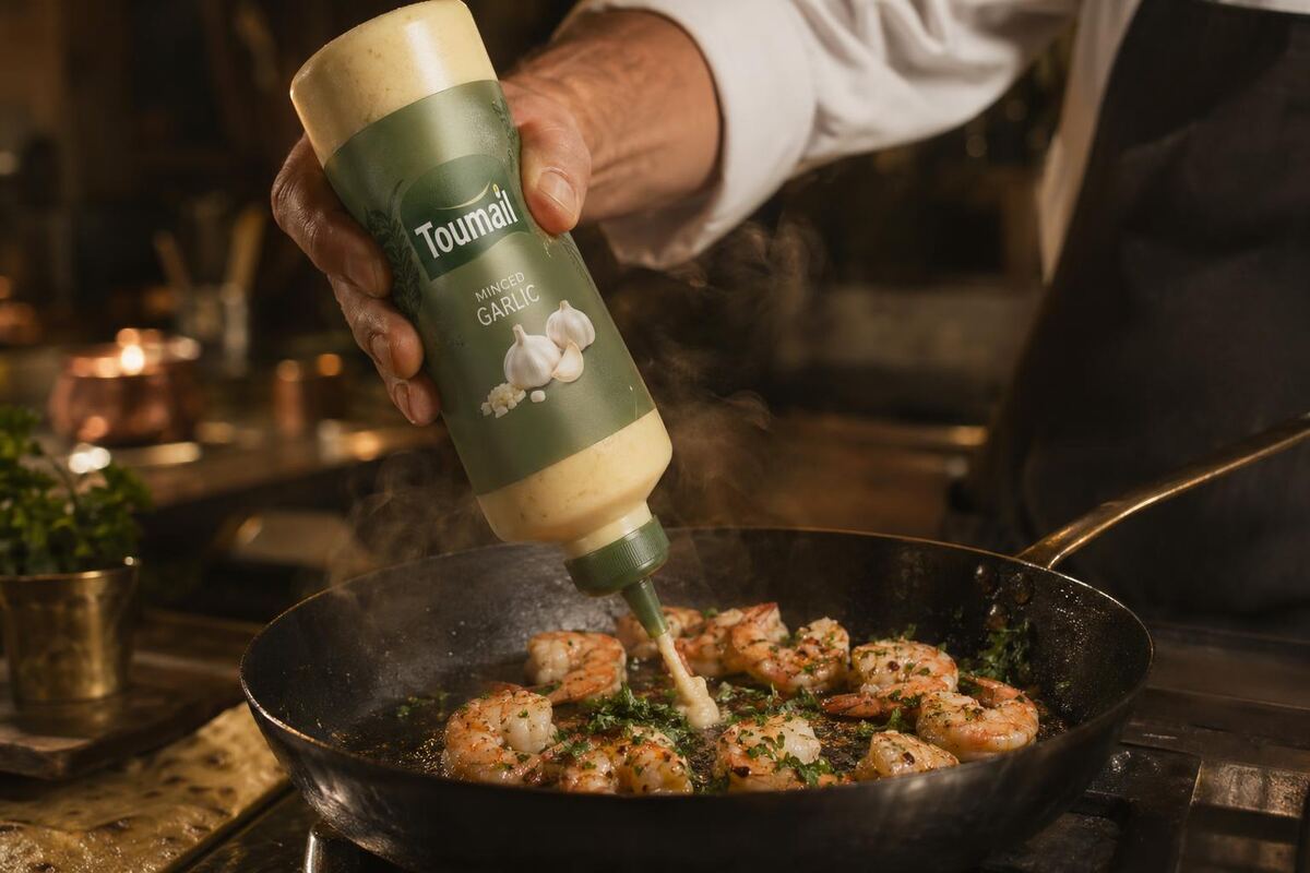 Chef squeezing Toumail minced garlic into a hot pan with shrimp